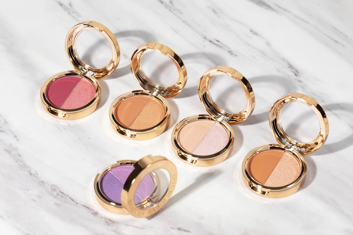 Close-up of 5 nude-tone dual-color private label eyeshadow palettes with gold packaging and shimmer finish, displayed on a white marble-patterned background