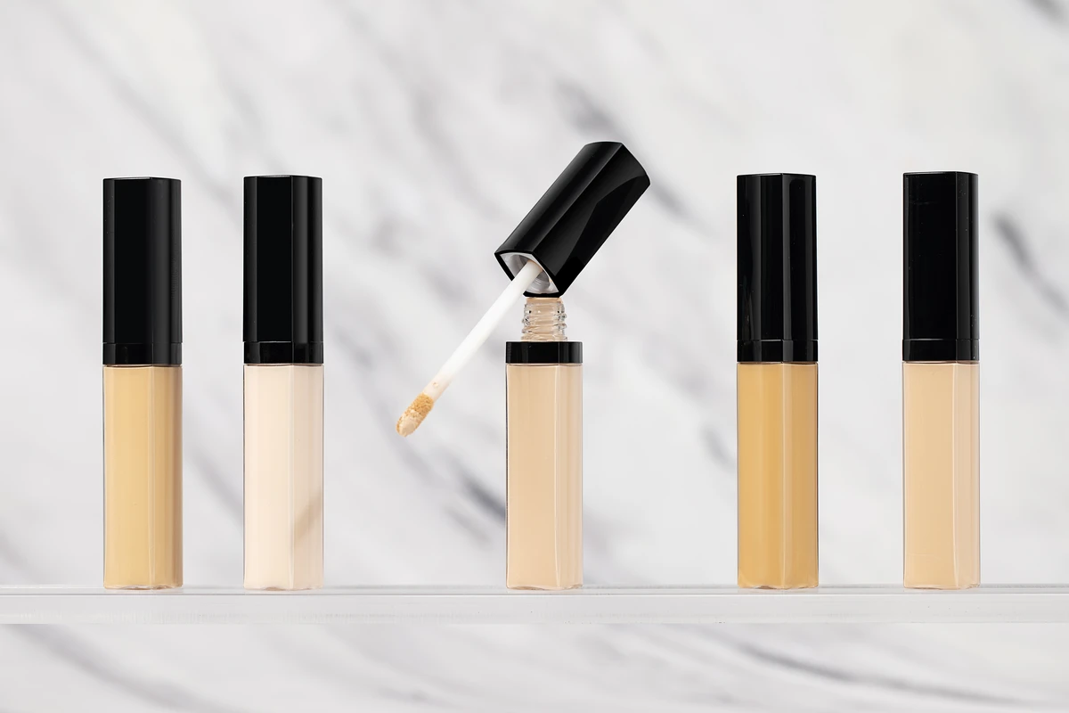 Close-up of 5 skin-tone liquid concealers with square caps, featuring smooth application and full coverage, set against a white marble-patterned background