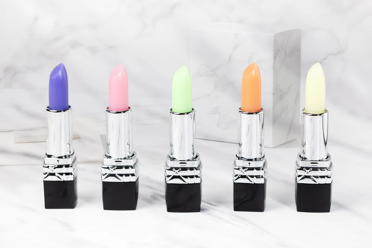 Close-up of private label color-changing lip balms in nude tones with square black tubes, set against a marble-patterned background