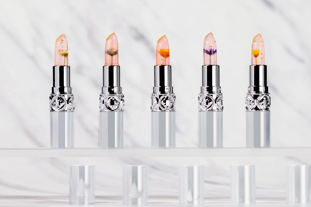 Close-up of private label color-changing infused lip balms in nude tones with round silver tubes, set against a marble-patterned background